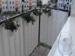 Biała osłona balkonowa na wymiar zamontowana na balustradzie, ozdobiona wiszącymi doniczkami z białymi kwiatami.