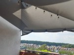 Szary żagiel ogrodowy wodoszczelny premium 2x2 rozpięty na balkonie, ozdobiony girlandą świetlną z żarówkami.