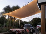 Beżowy żagiel przeciwsłoneczny wodoszczelny premium 3x4 m nad tarasem z girlandą świetlną wieczorem.