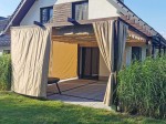 Brązowa pergola tarasowa z zamontowaną beżową roletą rzymską poziomą premium Decor 3x5 oraz zasłonami ogrodowymi.