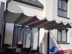Szara roleta rzymska pozioma premium Decor 4x4 zamontowana nad tarasem obok szarych mebli ogrodowych i huśtawki.