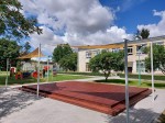 Żagiel przeciwsłoneczny trójkątny HDPE 4,2x4,2x5,9 m zamontowany nad drewnianym tarasem na placu zabaw.