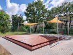 Trójkątny piaskowy żagiel przeciwsłoneczny HDPE 4,2x4,2x5,9 m zamontowany nad drewnianym tarasem w ogrodzie.
