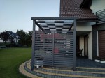 Szary pas altanowy przeciwsłoneczny 1x5 m zamontowany na nowoczesnej pergoli tarasowej przy domu.
