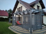 Szary pas altanowy przeciwsłoneczny 1x5 zamontowany na nowoczesnej pergoli drewnianej przy tarasie domu jednorodzinnego.