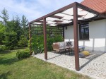 Brązowa pergola tarasowa osłonięta białym pasem altanowym przeciwsłonecznym, pod którą stoją meble ogrodowe.