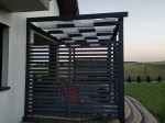 Grafitowa pergola tarasowa z przesuwnym, biało-czarnym pasem altanowym przeciwsłonecznym o wymiarach 1x5 m.