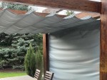 Pozioma roleta rzymska premium Decor o wymiarach 3x5 m zamontowana na drewnianej pergoli w ogrodzie.
