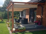 Beżowa roleta rzymska pozioma premium Decor 4x4 zamontowana na drewnianej pergoli nad tarasem z meblami ogrodowymi.
