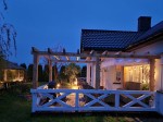 Roleta rzymska pozioma premium Decor zainstalowana na drewnianej pergoli przy tarasie domu wieczorową porą.