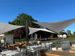 Białe żagle wodoszczelne premium w kształcie trójkąta, zamontowane na tarasie restauracji jako zadaszenie.