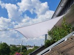 Wodoszczelny żagiel ogrodowy premium 2x2 w kolorze białym zamontowany na tarasie na tle nieba i panoramy miasta.