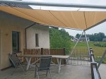 Żagiel przeciwsłoneczny HDPE 5x6m zamontowany na tarasie nad stołem i krzesłami, chroniący przed słońcem w ogrodzie.