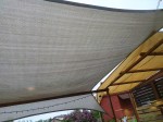 Beżowy żagiel przeciwsłoneczny HDPE o wymiarach 5x6 metrów zamontowany nad drewnianym tarasem w ogrodzie.