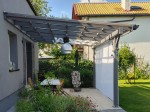 Jasnoszary żagiel przeciwsłoneczny rozsuwany o wymiarach 2x5 m zamontowany pod konstrukcją nowoczesnej pergoli.