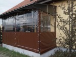 Przeźroczysta osłona tarasowa na wymiar z brązowym pasem materiału, zamontowana na zadaszonym tarasie domu.