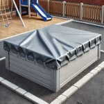 Szara plandeka na wymiar zabezpieczająca piaskownicę wykonaną z desek kompozytowych na placu zabaw.