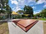 Żółty trójkątny żagiel przeciwsłoneczny HDPE 3x3x4,2 nad drewnianym podestem na placu zabaw.