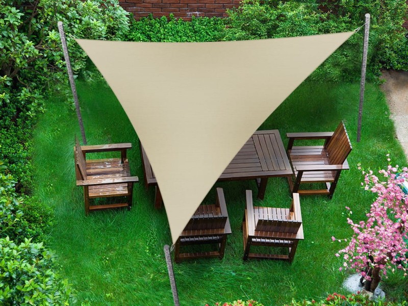 Trójkątny żagiel ogrodowy w kolorze beżowym zamontowany nad drewnianymi meblami ogrodowymi na zielonej trawie.