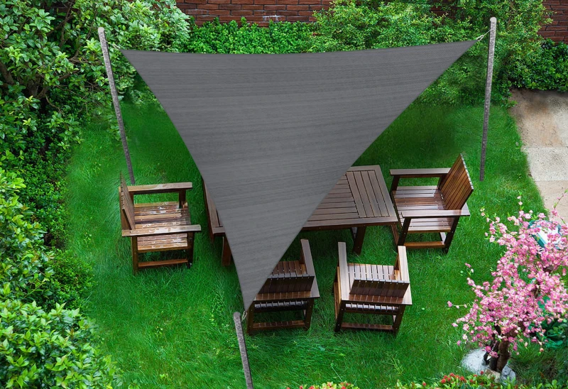 Szary trójkątny żagiel przeciwsłoneczny HDPE o wymiarach 4,2x4,2x5,9 m rozpięty nad meblami ogrodowymi na trawniku.
