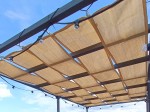 Beżowy pas altanowy przeciwsłoneczny HDPE 0,4x5m zamontowany na metalowej konstrukcji pergoli z lampkami.
