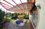 Biała pozioma roleta rzymska na taras o wymiarach 2,40x6,60 m, zamontowana pod drewnianą pergolą nad meblami ogrodowymi.