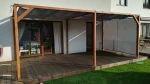 Zasłona tarasowa o wymiarach 4,90x1,90 m, wzór 72, zamontowana na drewnianej pergoli nad tarasem z desek.
