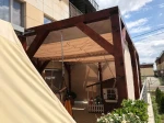 Drewniana pergola z zamontowaną szarą zasłoną z materiału meshflag osłaniającą taras przed słońcem i sąsiadami.