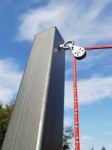Bloczek z knagą do montażu żagli przeciwsłonecznych zamocowany na stalowym słupku z czerwoną liną na tle nieba.