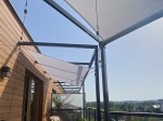 Biały, prostokątny żagiel wodoszczelny premium 1x2 m zamontowany na metalowej konstrukcji tarasu z lampkami.