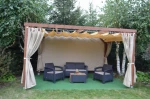 Beżowa zasłona boczna Mesh Flag na drewnianej pergoli tarasowej, osłaniająca meble ogrodowe w otoczeniu zieleni.