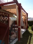 Beżowa zasłona tarasowa 2,29x3,70 m zamontowana na drewnianej pergoli z materiałowym zadaszeniem nad patio.