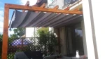 Popielata roleta rzymska pozioma zamontowana na drewnianej pergoli nad tarasem z meblami ogrodowymi.