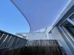 Biały żagiel wodoszczelny balkonowy o wymiarach 1,00x1,35 m zamontowany na tarasie nad drewnianą osłoną.