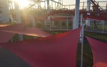 Czerwony żagiel ogrodowy wodoszczelny premium 3,5x3,5x3,5 m zamontowany nad ścieżką w parku rozrywki.