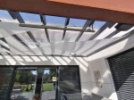 Trójkątny żagiel ogrodowy wodoszczelny premium 4,2x4,2x5,9 zamontowany pod przeszklonym dachem nowoczesnego tarasu.