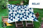 Wodoszczelny żagiel przeciwsłoneczny 3x4,5 w geometryczne trójkąty nad drewnianymi meblami ogrodowymi na trawniku.