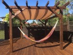Brązowa pergola z rozsuwanym wodoszczelnym żaglem ogrodowym 2,5x5 m, pod którym wisi kolorowy hamak.
