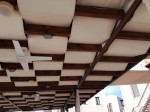 Wodoszczelny biały pas altanowy 0,5x5 m zamontowany na drewnianej pergoli tarasowej z widocznym wentylatorem.