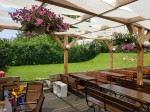 Biały pas altanowy przeciwsłoneczny na drewnianej konstrukcji nad stolikami i ławkami w ogródku restauracyjnym.
