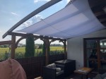 Wodoszczelny żagiel ogrodowy premium 4x4m w kolorze białym zamontowany na drewnianej pergoli nad tarasem.