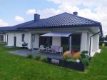 Szary ogrodowy żagiel wodoszczelny na wymiar zamontowany nad tarasem nowoczesnego domu jednorodzinnego.