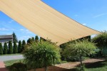 Beżowy prostokątny żagiel przeciwsłoneczny HDPE 5x6m rozwieszony nad ogrodem zapewnia cień nad krzewami i ścieżką.