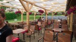 Biały pas altanowy przeciwsłoneczny na wymiar zamontowany na drewnianej konstrukcji ogródka restauracyjnego.