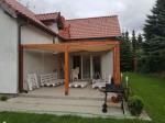 Wodoszczelny żagiel rozsuwany zamontowany na drewnianej pergoli tarasowej przy domu jednorodzinnym.