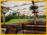 Biały pas altanowy przeciwsłoneczny 1x5 m zamontowany na drewnianej pergoli w ogródku restauracyjnym.