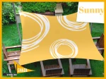 Żółty wodoszczelny żagiel ogrodowy 3x4 m w białe wzory nad drewnianymi meblami na trawniku. Producen Sunshade.