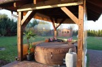 Przeźroczysta osłona tarasowa na wymiar osłaniająca altanę drewnianą z dmuchanym jacuzzi i rośliną doniczkową.
