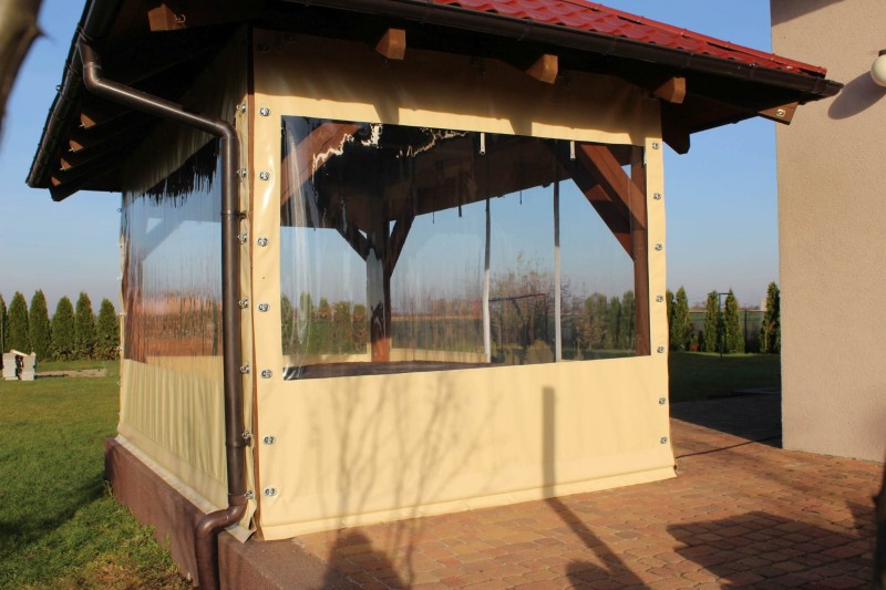 Przezroczysta osłona tarasowa na wymiar z beżowym obramowaniem, zamontowana na drewnianej altanie ogrodowej.