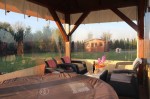 Przezroczysta osłona tarasowa na wymiar zamontowana na drewnianej altanie z meblami ogrodowymi i jacuzzi.